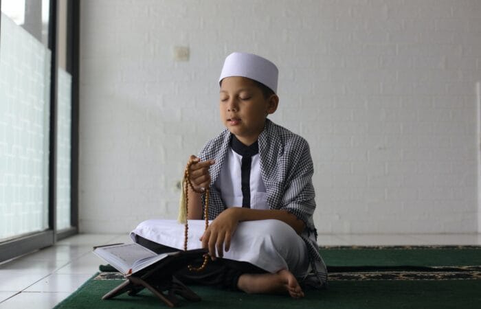 Zikir: Pengertian, Jenis, dan Keutamaan Muslim boy praying using prayer beads