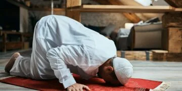 Middle Eastern man performing ritual prayer on the floor at home.