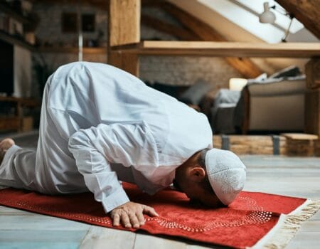 Middle Eastern man performing ritual prayer on the floor at home.